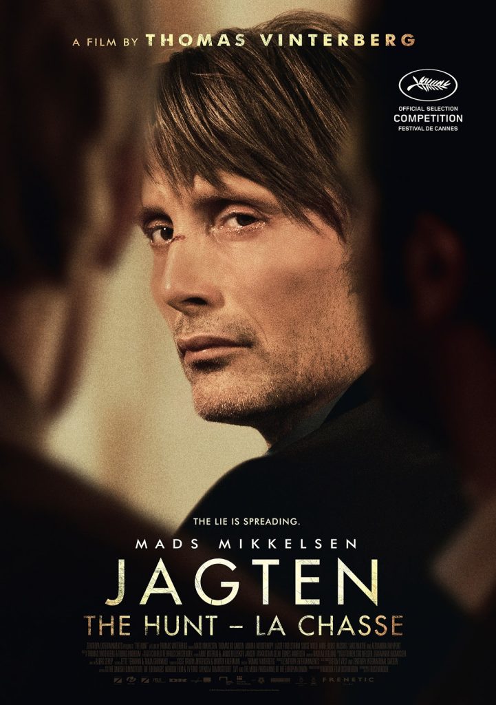 Filmposter van Jagten: een man kijkt wat treurig over zijn schouder de kijker aan tussen twee andere mensen door.